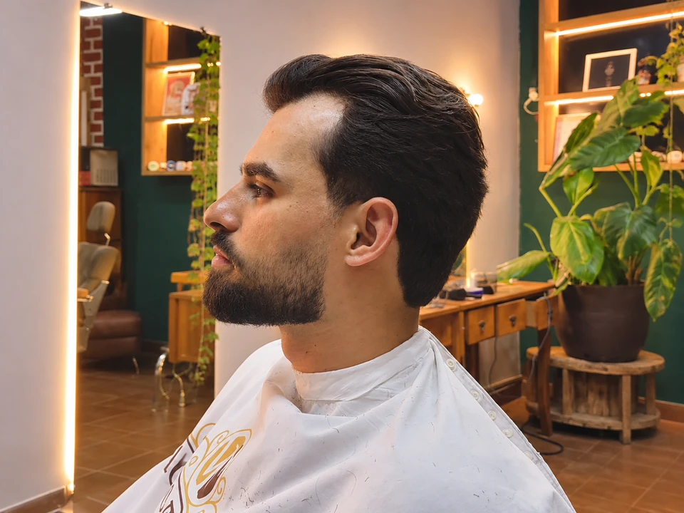 Cliente da barbearia com cabelo penteado e barba alinhada, em vista de perfil.